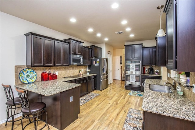 kitchen featuring sink, stainless steel appliances, pendant lighting, decorative backsplash, and light wood-type flooring