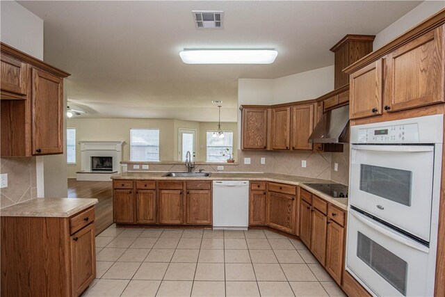 kitchen featuring white appliances, backsplash, wall chimney range hood, sink, and decorative light fixtures