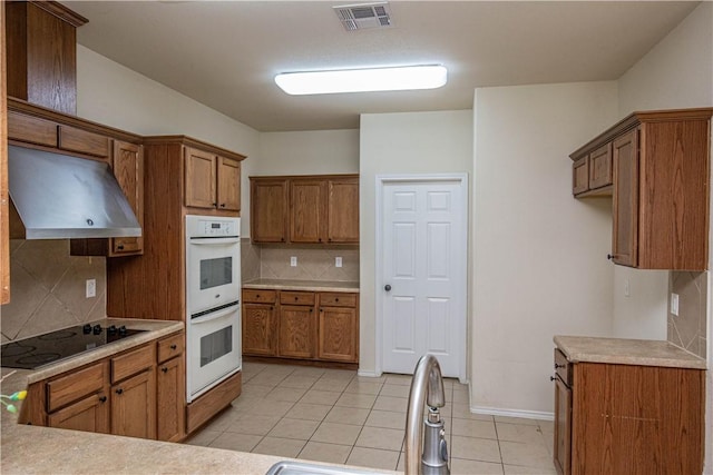 kitchen with white double oven, range hood, electric cooktop, decorative backsplash, and light tile patterned floors