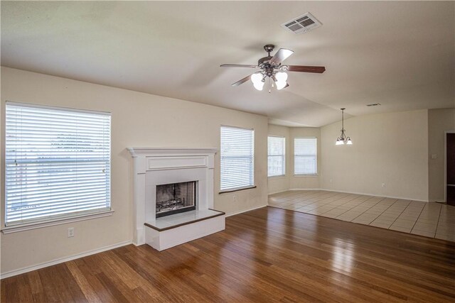 unfurnished living room featuring ceiling fan with notable chandelier, dark hardwood / wood-style flooring, and vaulted ceiling