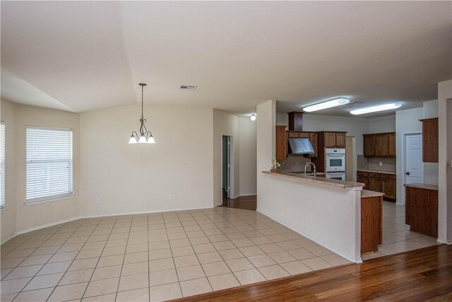 kitchen featuring lofted ceiling, light wood-type flooring, double oven, decorative light fixtures, and kitchen peninsula