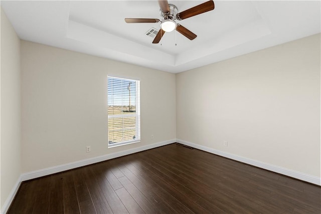 spare room featuring dark hardwood / wood-style flooring, a tray ceiling, and ceiling fan