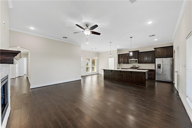 kitchen with appliances with stainless steel finishes, ornamental molding, dark hardwood / wood-style floors, hanging light fixtures, and an island with sink