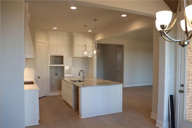 kitchen with sink, hanging light fixtures, white cabinets, and a center island with sink