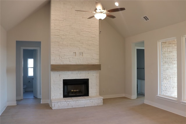 unfurnished living room featuring vaulted ceiling, ceiling fan, a stone fireplace, and light hardwood / wood-style floors