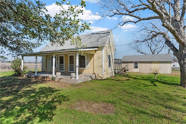 back of house with a patio area, a shingled roof, a lawn, and an outbuilding