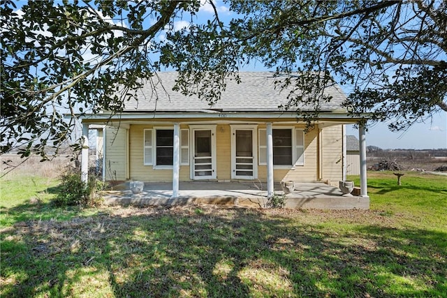 view of front facade with a patio area, a shingled roof, and a front lawn