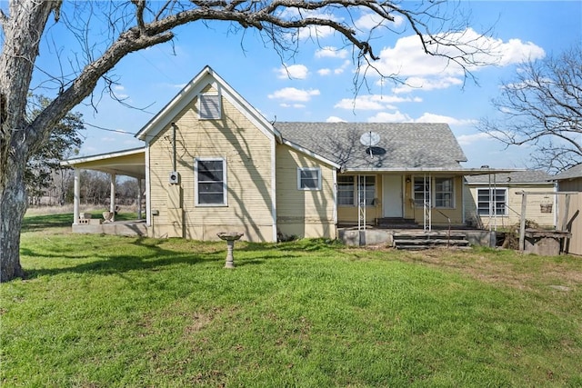 back of house with covered porch, roof with shingles, an attached carport, and a yard