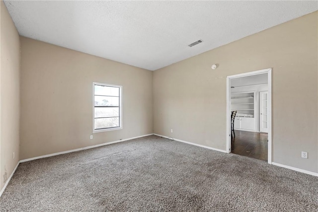 spare room featuring a textured ceiling, carpet floors, visible vents, and baseboards