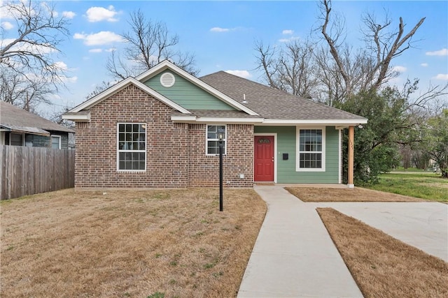 ranch-style house with roof with shingles, fence, a front lawn, and brick siding