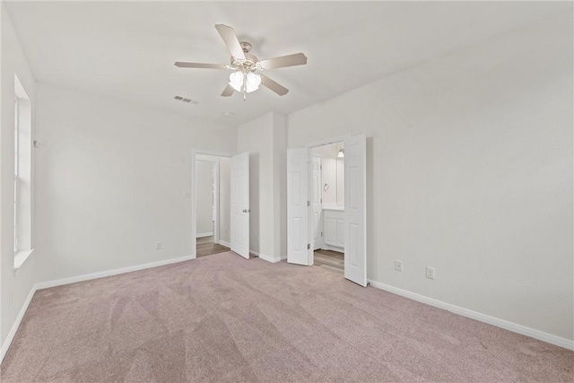 unfurnished bedroom with baseboards, visible vents, a ceiling fan, ensuite bath, and carpet