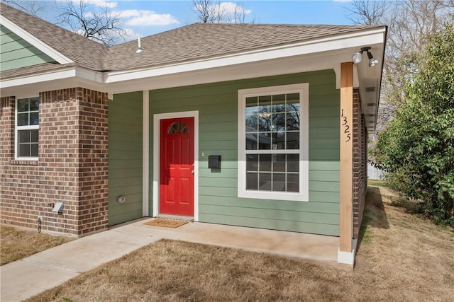 property entrance with roof with shingles, a porch, and brick siding