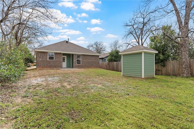 rear view of house with fence, an outdoor structure, a lawn, and brick siding