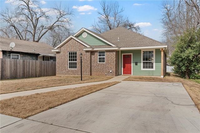 view of front of house with a shingled roof, fence, a front lawn, and brick siding