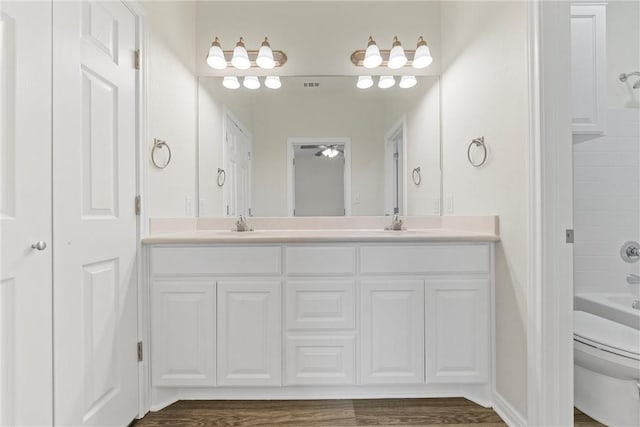 bathroom with double vanity, visible vents, toilet, a sink, and wood finished floors