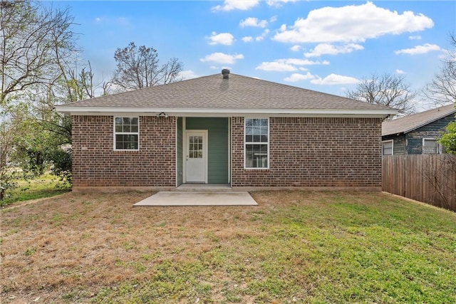 rear view of property featuring a shingled roof, a patio, fence, a yard, and brick siding