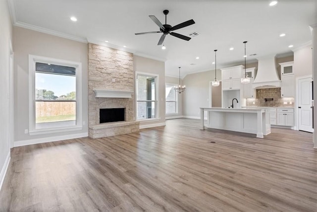 unfurnished living room with ceiling fan with notable chandelier, sink, light wood-type flooring, a fireplace, and ornamental molding