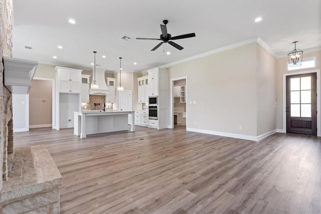 unfurnished living room with ceiling fan with notable chandelier, light hardwood / wood-style floors, and ornamental molding