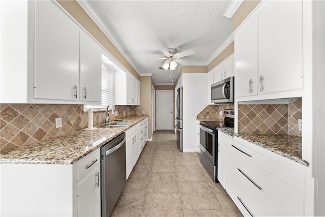 kitchen with appliances with stainless steel finishes, light stone counters, crown molding, white cabinetry, and a sink