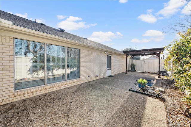 view of home's exterior with roof with shingles, brick siding, a patio area, fence, and a pergola