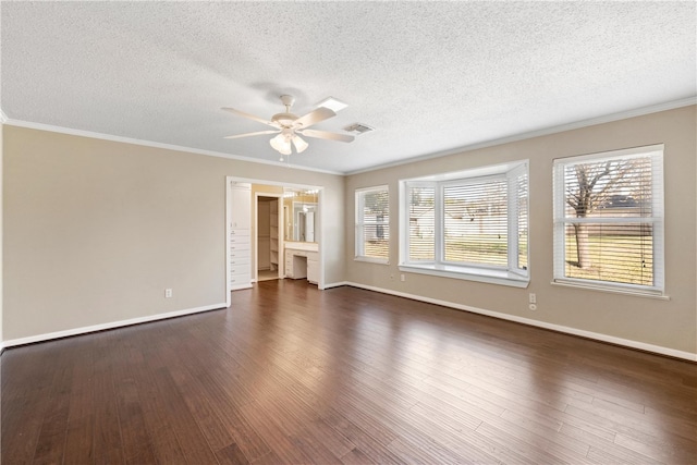 empty room with visible vents, dark wood-type flooring, ornamental molding, a ceiling fan, and baseboards