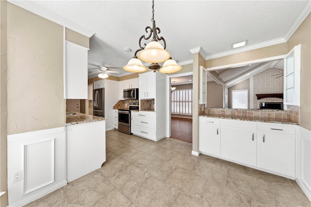 kitchen featuring lofted ceiling, a wainscoted wall, hanging light fixtures, stainless steel appliances, and white cabinetry