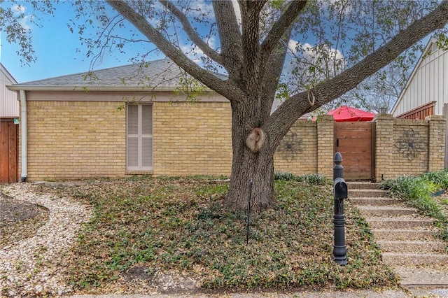 view of home's exterior featuring a shingled roof, fence, and brick siding