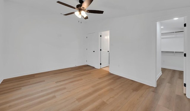 unfurnished bedroom featuring baseboards, a walk in closet, and light wood-style floors