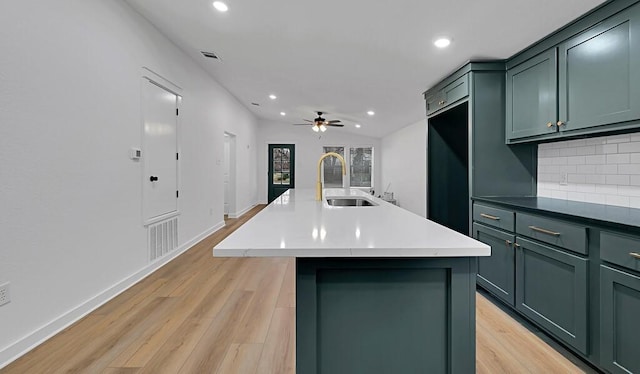 kitchen with visible vents, light wood-style flooring, an island with sink, a sink, and decorative backsplash