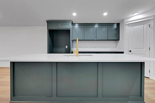 kitchen featuring light countertops, tasteful backsplash, light wood finished floors, and a sink