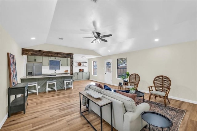 living room with lofted ceiling, ceiling fan, light wood-style flooring, and baseboards