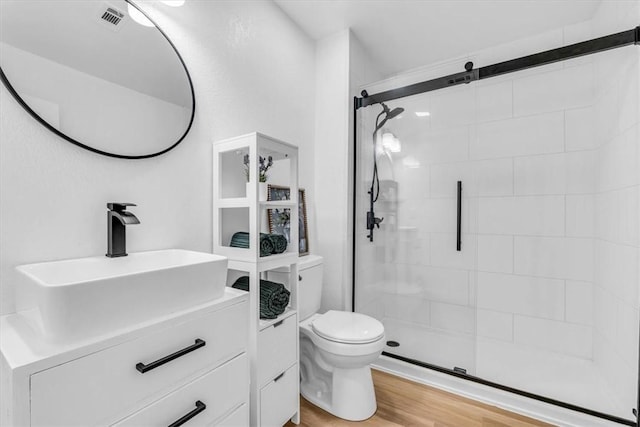 full bath featuring toilet, wood finished floors, vanity, visible vents, and a shower stall