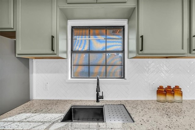 kitchen with green cabinetry, a sink, light stone countertops, and decorative backsplash