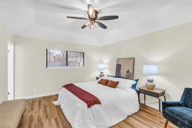 bedroom featuring ceiling fan, a tray ceiling, wood finished floors, and baseboards