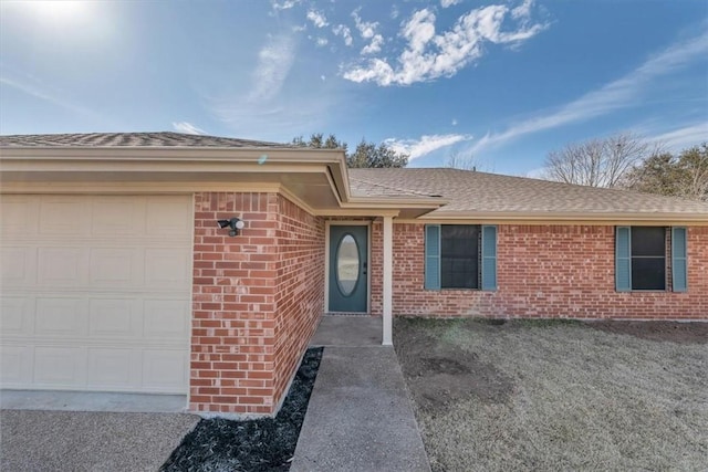 doorway to property with a garage, brick siding, and roof with shingles