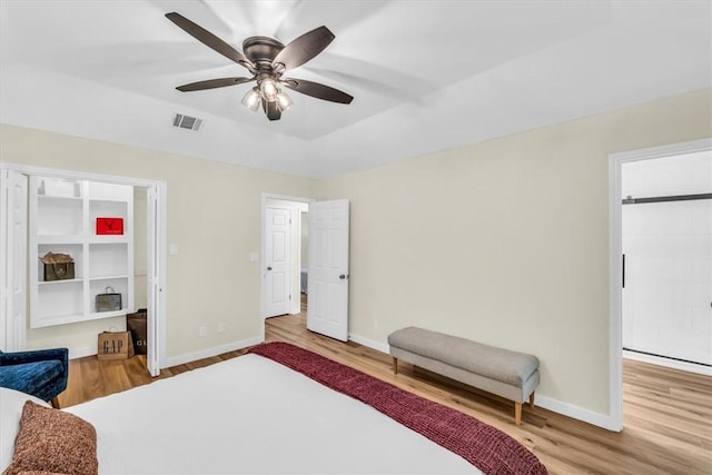 bedroom with a raised ceiling, wood finished floors, visible vents, and baseboards