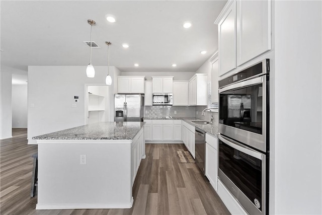 kitchen featuring white cabinets, hanging light fixtures, a kitchen island, wood-type flooring, and stainless steel appliances