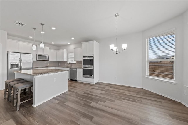 kitchen featuring white cabinets, appliances with stainless steel finishes, decorative light fixtures, and a kitchen island