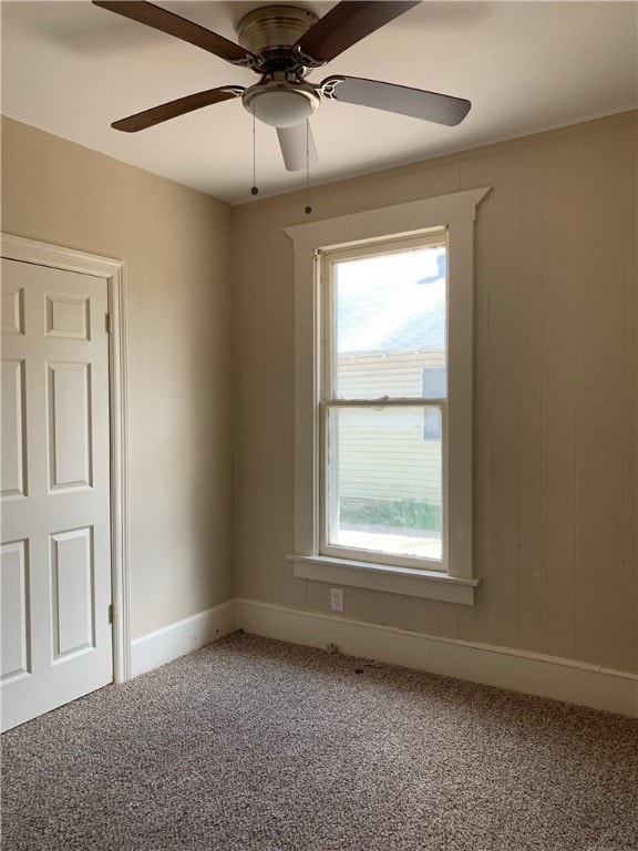 carpeted empty room with ceiling fan and wooden walls