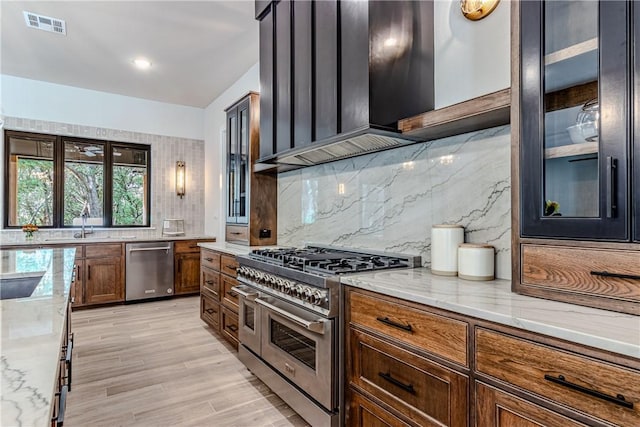 kitchen with light stone counters, light hardwood / wood-style flooring, backsplash, stainless steel appliances, and wall chimney range hood