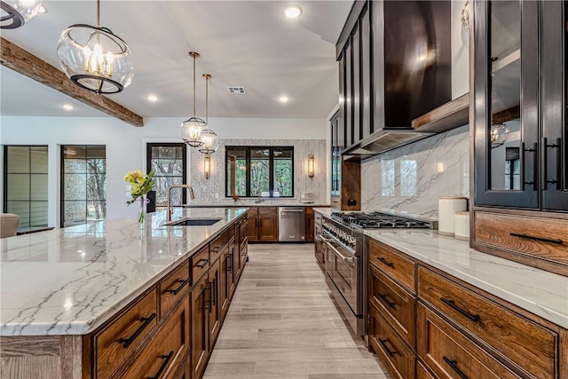 kitchen with appliances with stainless steel finishes, decorative light fixtures, tasteful backsplash, sink, and a large island with sink