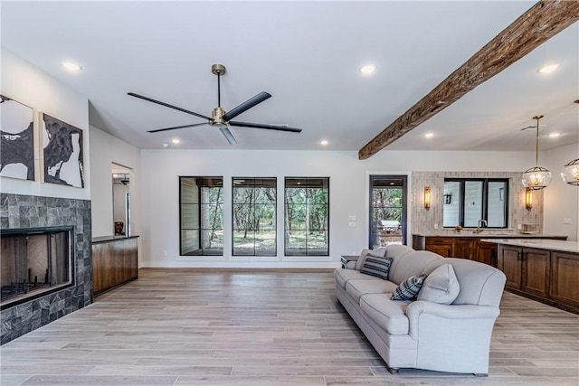 living room featuring sink, ceiling fan, a fireplace, light hardwood / wood-style floors, and beamed ceiling