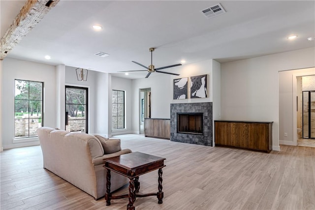 living room with a tile fireplace, ceiling fan, and light wood-type flooring