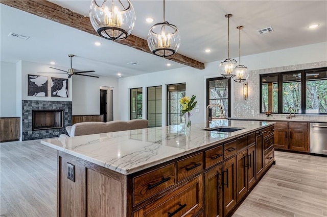 kitchen featuring a spacious island, sink, decorative light fixtures, dishwasher, and light stone countertops