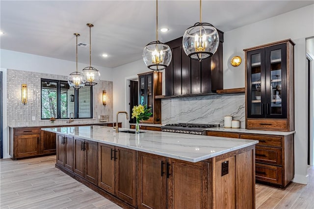 kitchen featuring light stone counters, sink, a center island with sink, and pendant lighting