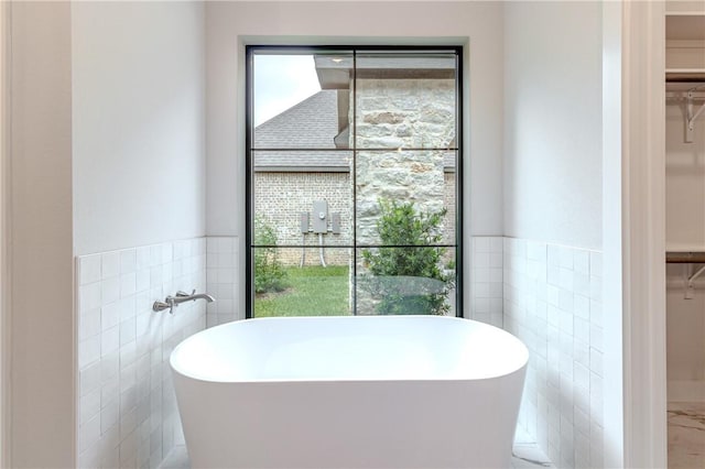 bathroom featuring tile walls, a tub, and a healthy amount of sunlight