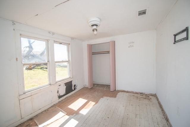 unfurnished bedroom featuring light wood-style flooring, visible vents, and a closet