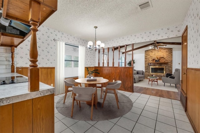 dining area with lofted ceiling, light tile patterned flooring, a textured ceiling, and a brick fireplace