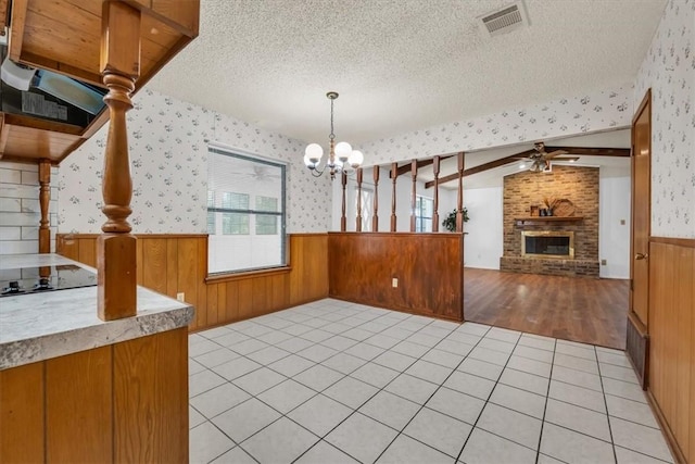 kitchen with vaulted ceiling, a textured ceiling, a fireplace, decorative light fixtures, and light hardwood / wood-style floors