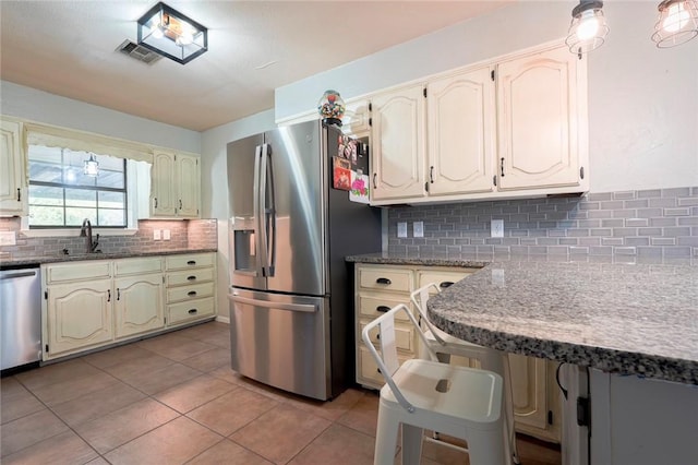 kitchen with sink, decorative backsplash, appliances with stainless steel finishes, light tile patterned flooring, and light stone counters